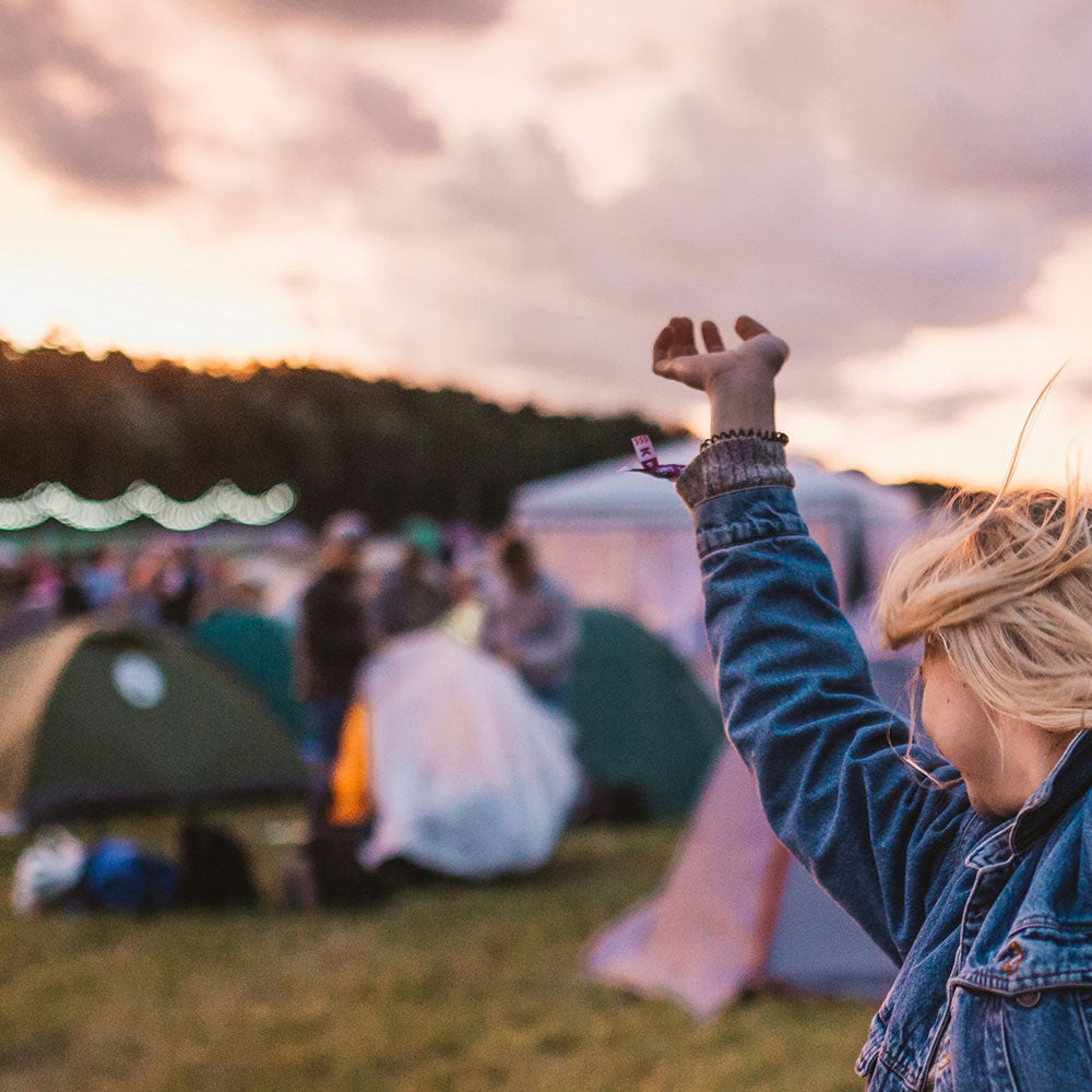Festival-Gängerin, die vor Zelten und Festival-Beleuchtung ausgelassen tanzt
