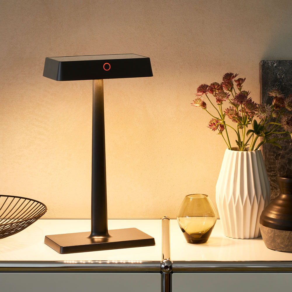 Schwarze Sigor Nucharge Akku-Tischleuchte, eingeschaltet, auf einem hellen Sideboard